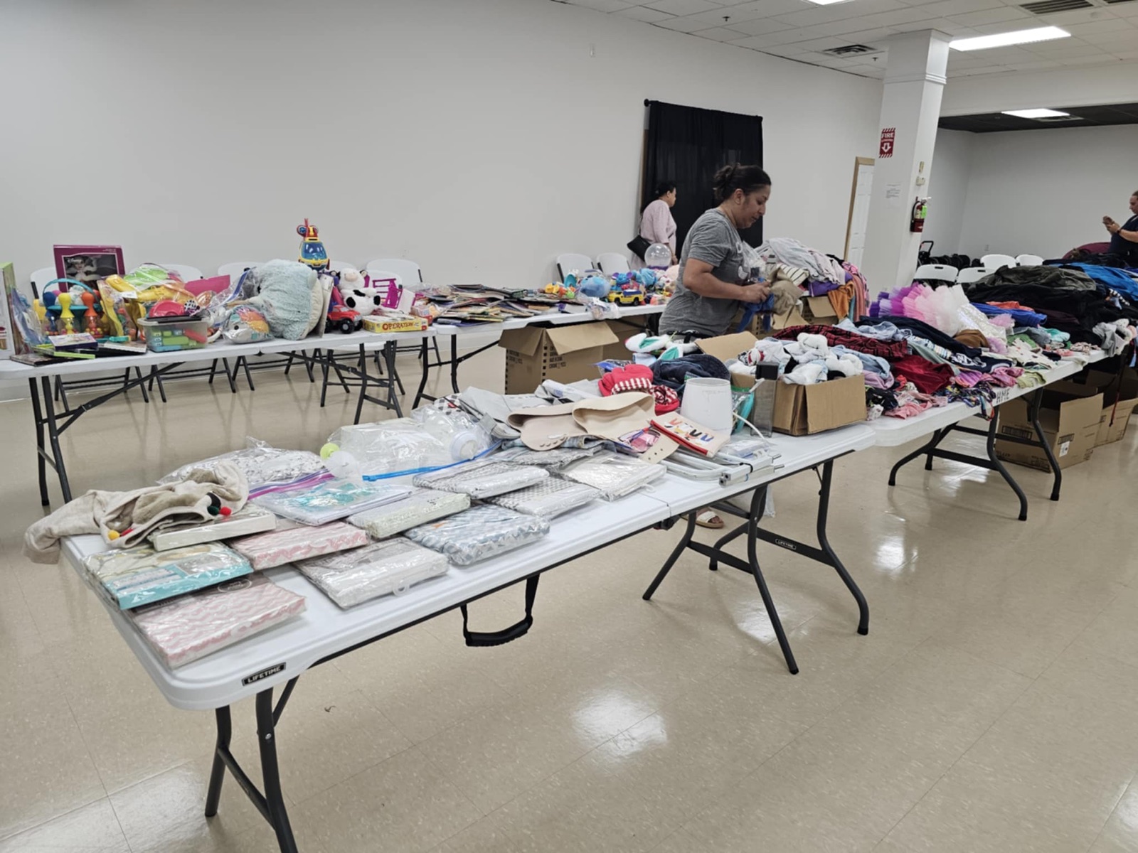 Volunteers sorting donated clothing, toys, and household essentials across long tables