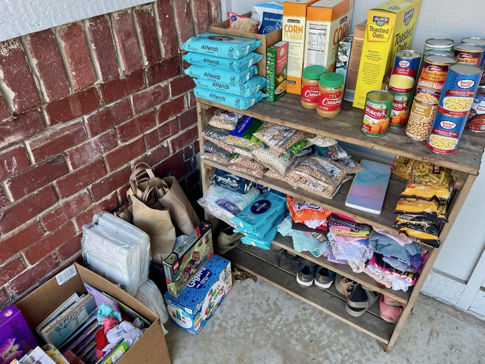 A stocked community pantry shelf with canned goods, cereal, diapers, and household items